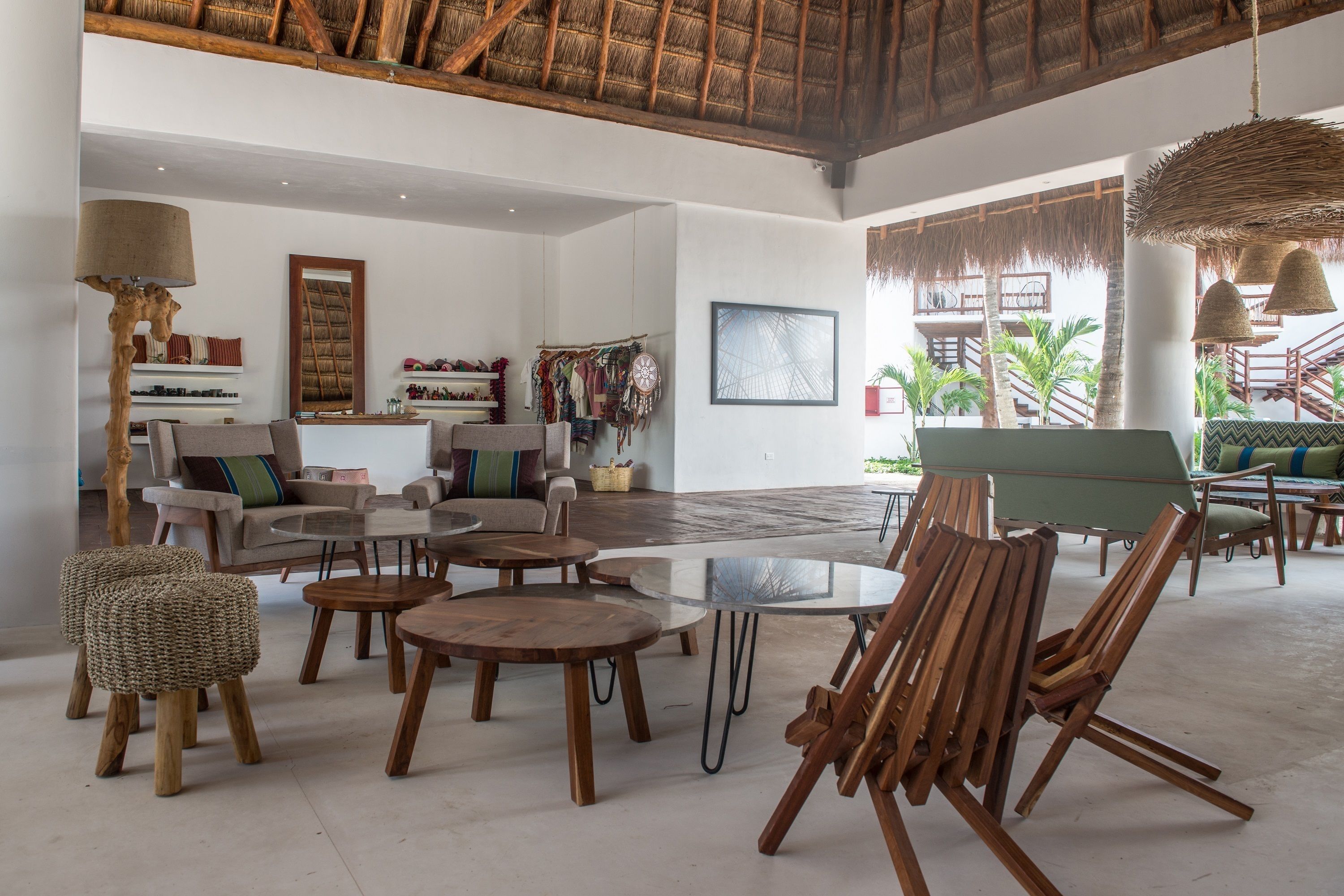 A spacious living area with a high ceiling, a large glass table, and several wooden chairs. There is a wardrobe with clothes and a mirror on the wall, and a hanging light fixture.