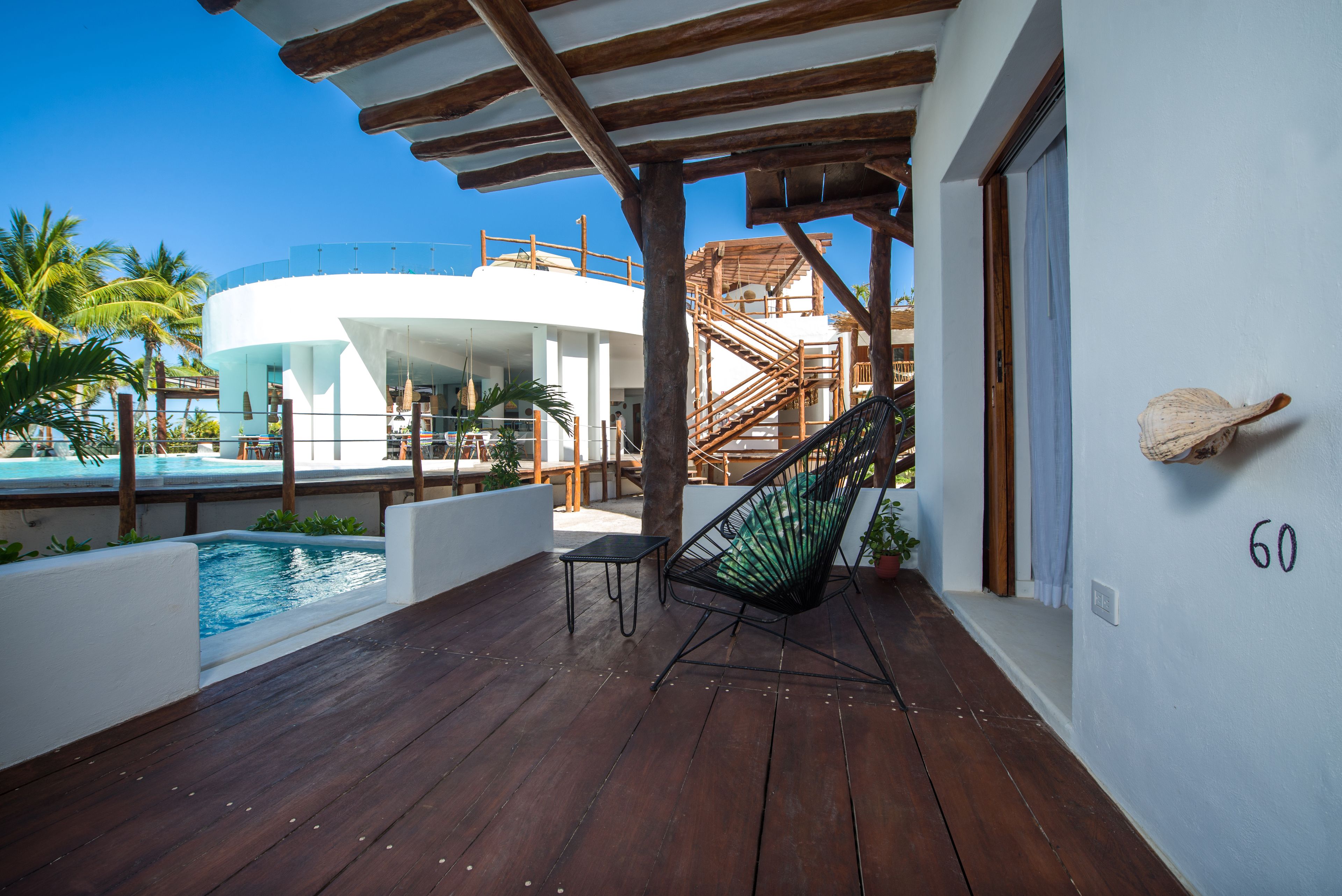 A wooden deck with a pool, a hammock, and a staircase leading to a building.