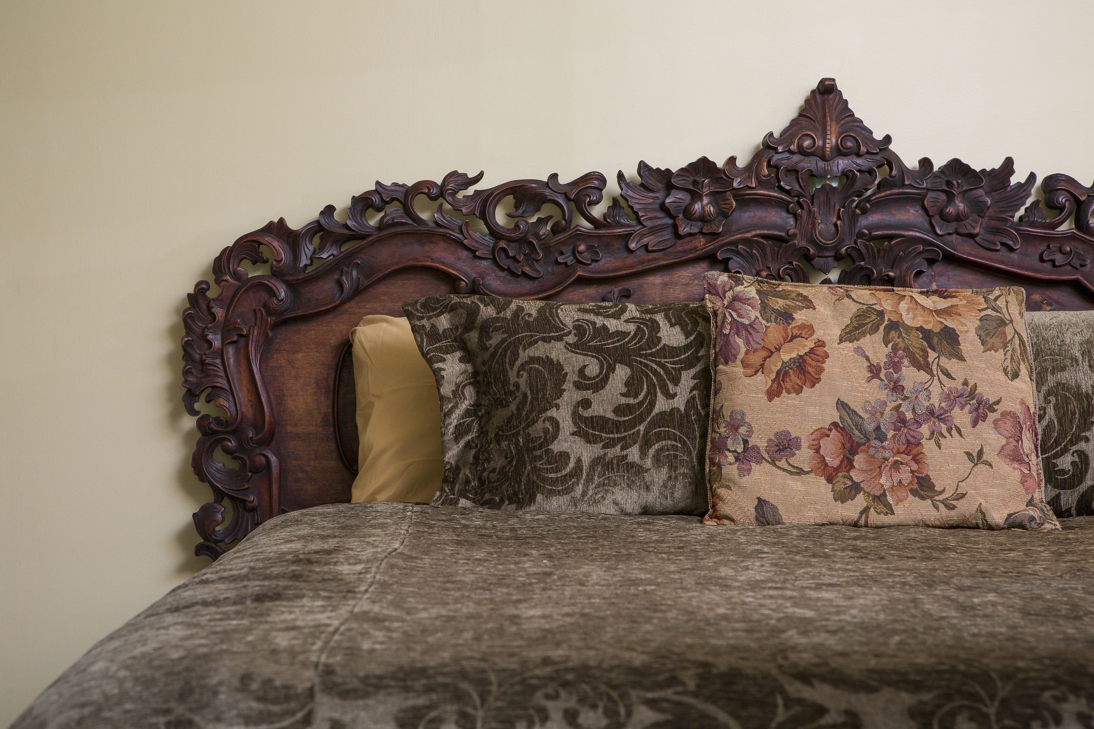 A bed with an ornate headboard, a floral-patterned pillow, and a plain pillow.