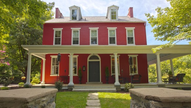 A red two-story house with a covered porch and a stone pathway leading to the entrance. - The Hollinger House (Lancaster)