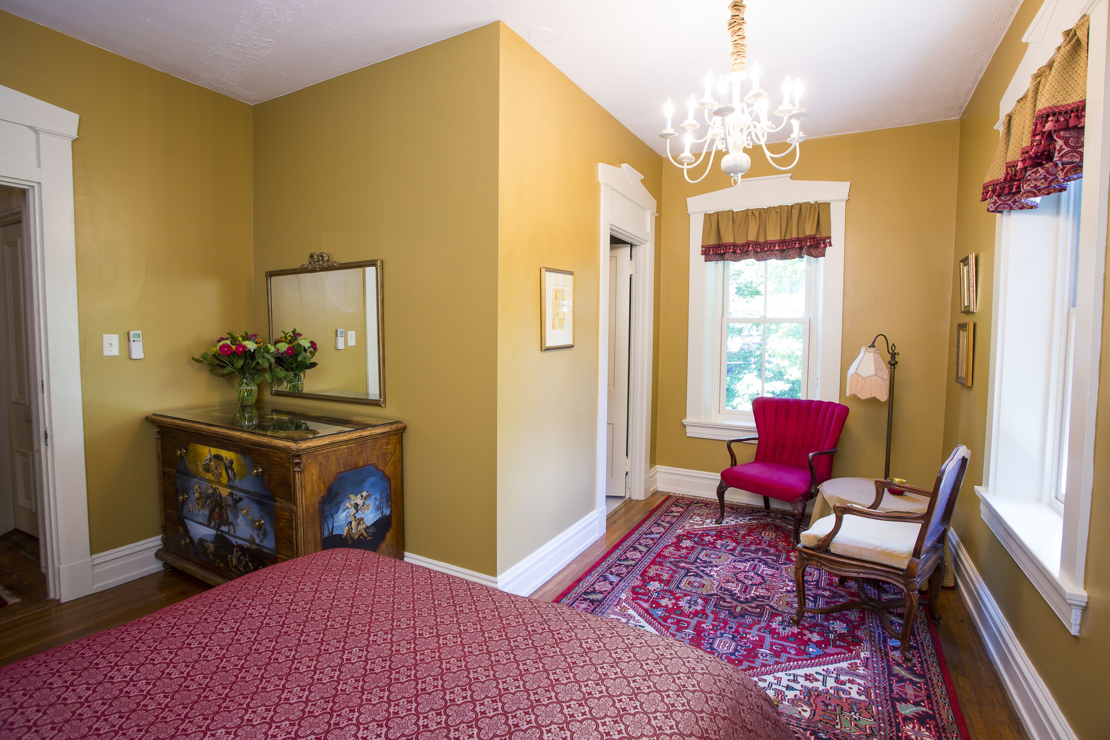 Une chambre à coucher comprenant un lit, une commode, un miroir, une chaise et une fenêtre avec des rideaux.