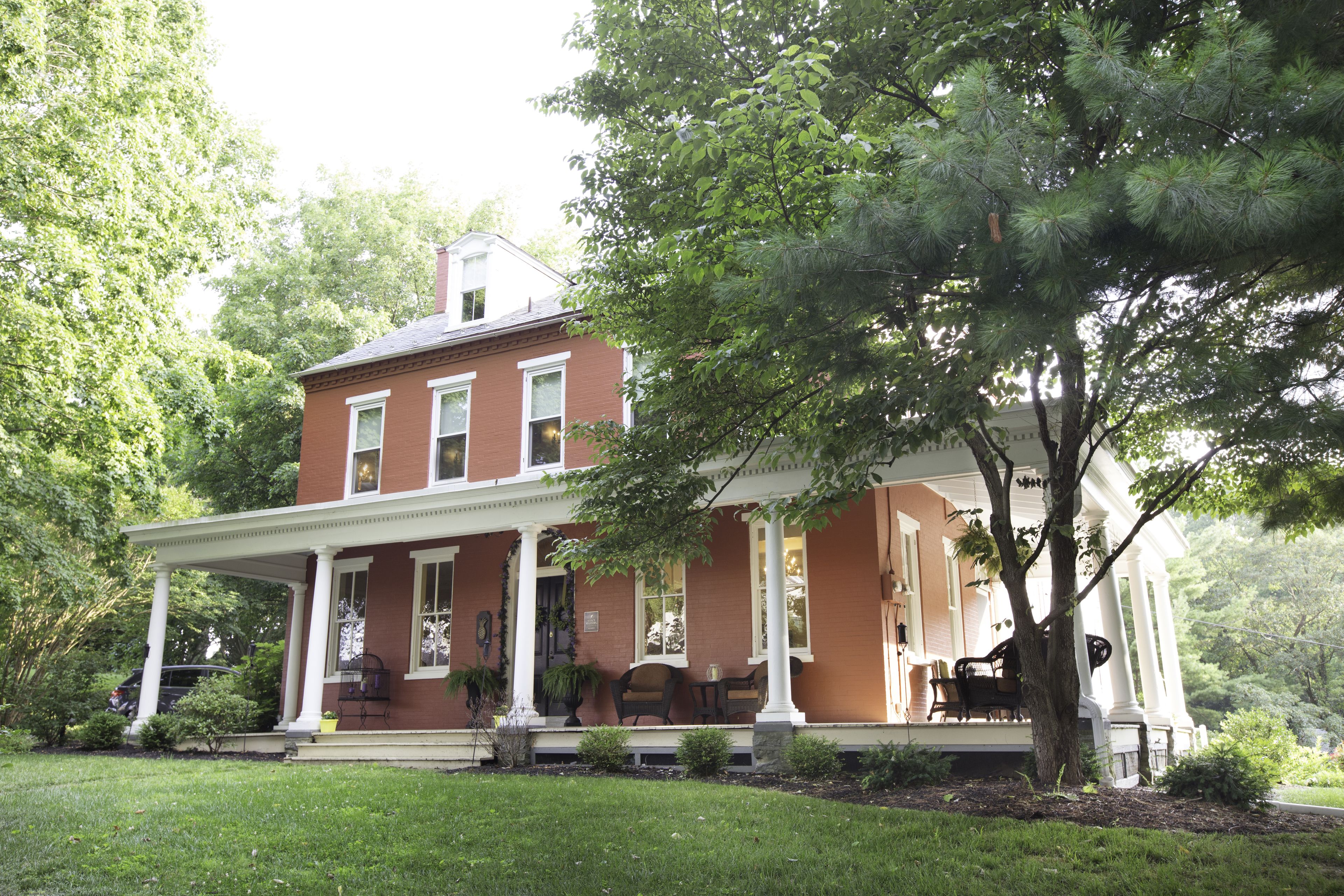 A two-story brick house with a covered porch and a large tree in front.