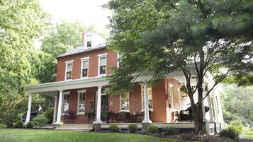 A two-story brick house with a covered porch and a large tree in front.