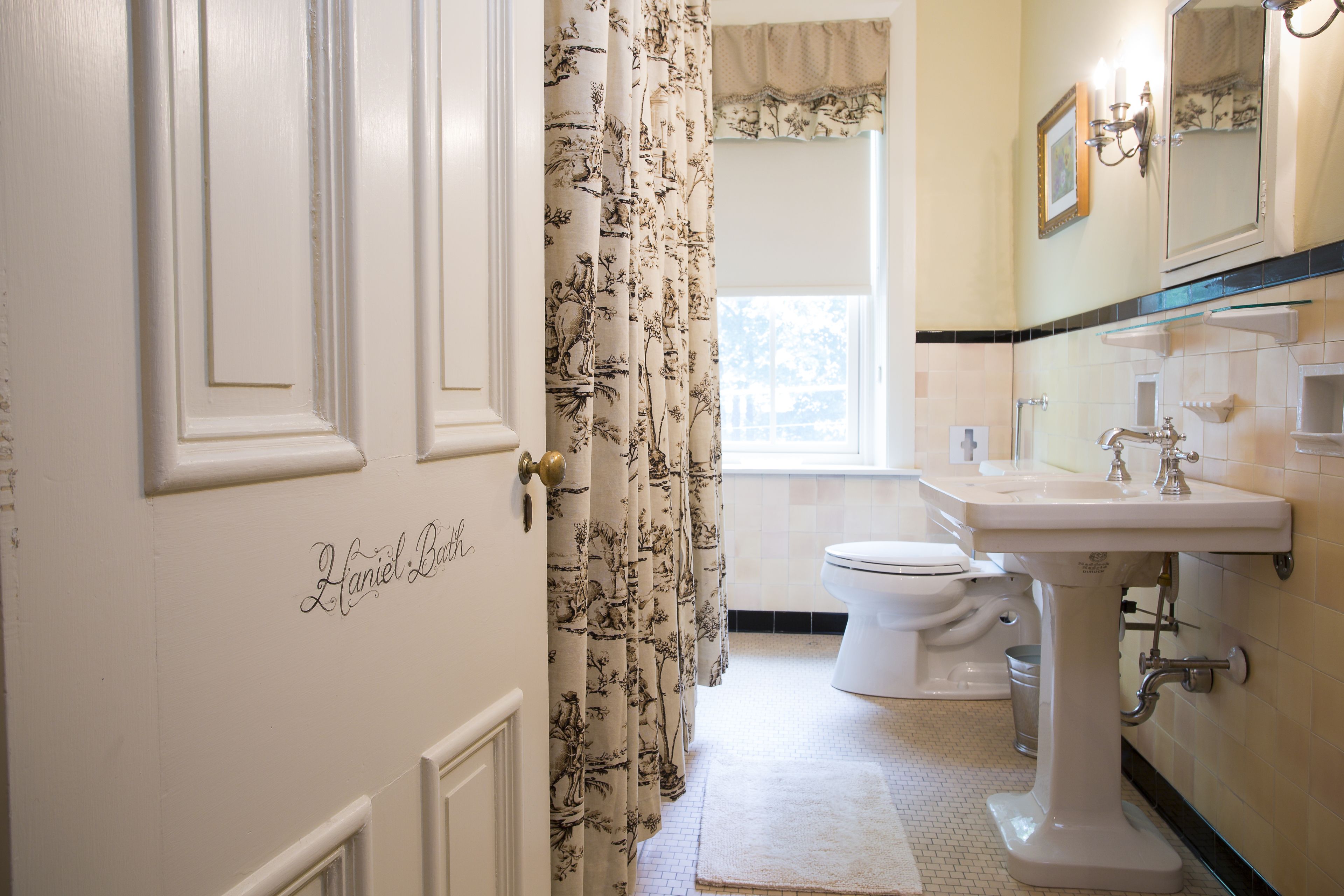 Une salle de bain avec une porte blanche, un lavabo, des toilettes et un rideau de douche à motifs floraux.