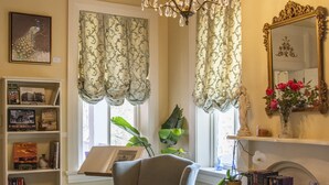 A cozy living room with a chandelier, bookshelves, a fireplace, and a large window with curtains. - The Hollinger House (Lancaster)