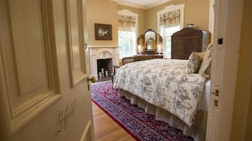 A bedroom with a large bed, a fireplace, a wooden dresser, and a red patterned rug.