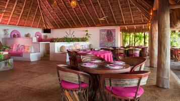 Un comedor interior con mesas y sillas de madera, techo de paja y un mural en la pared.