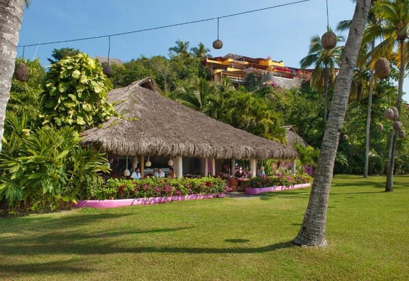 A thatched-roof structure surrounded by lush greenery and a well-maintained lawn. - Playa Rosa Bungalows (Costa Careyes)