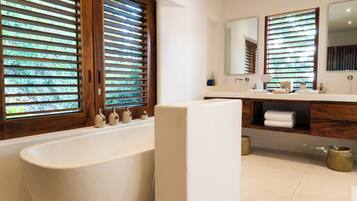 Un baño moderno con una bañera independiente, persianas de madera, un espejo grande y un mueble de tocador con lavamanos y toallero.