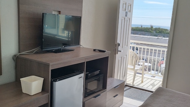 Une chambre d’hôtel compacte, dotée d’une télévision, d’un mini-réfrigérateur et d’un balcon donnant sur la rue.