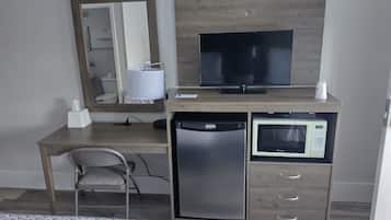 A hotel room with a wooden desk, a television, a microwave, a refrigerator, a chair, and a bed with patterned bedding.