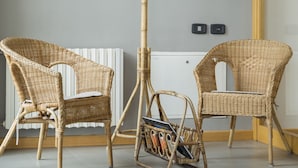 A room with two wicker chairs, a tall floor lamp, a poster on the wall, and a radiator. - La Cordata Accommodation - Zumbini 6 (Milan)