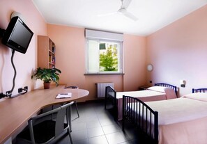 Un dormitorio con escritorio, televisor, ventana, radiador y cama.
