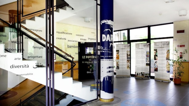 A modern interior with a staircase, a blue pillar with text, and informational posters. - La Cordata Accommodation - Zumbini 6 (Milan)