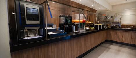 Una cocina moderna con cafetera, una exposición de frutas y una pared de vidrio.
