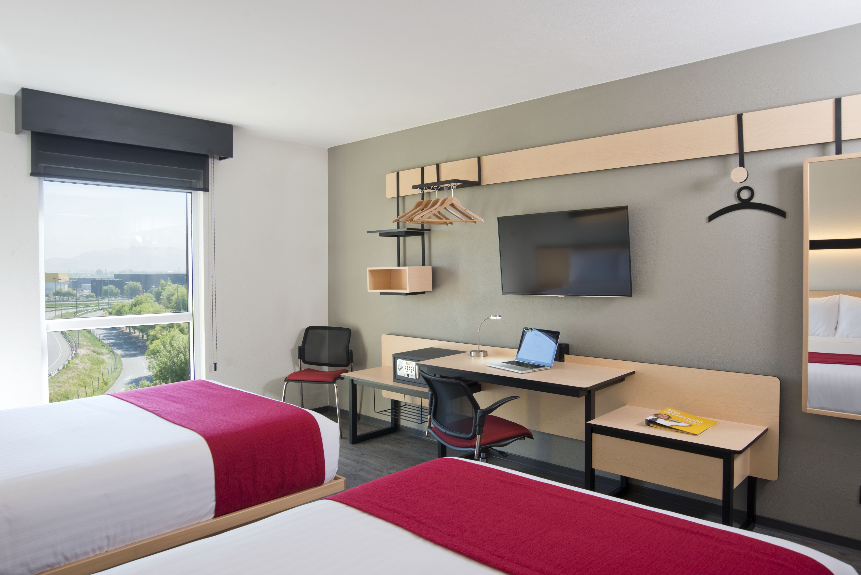 A hotel room with two beds, a desk with a laptop, a chair, a TV, and a wardrobe.