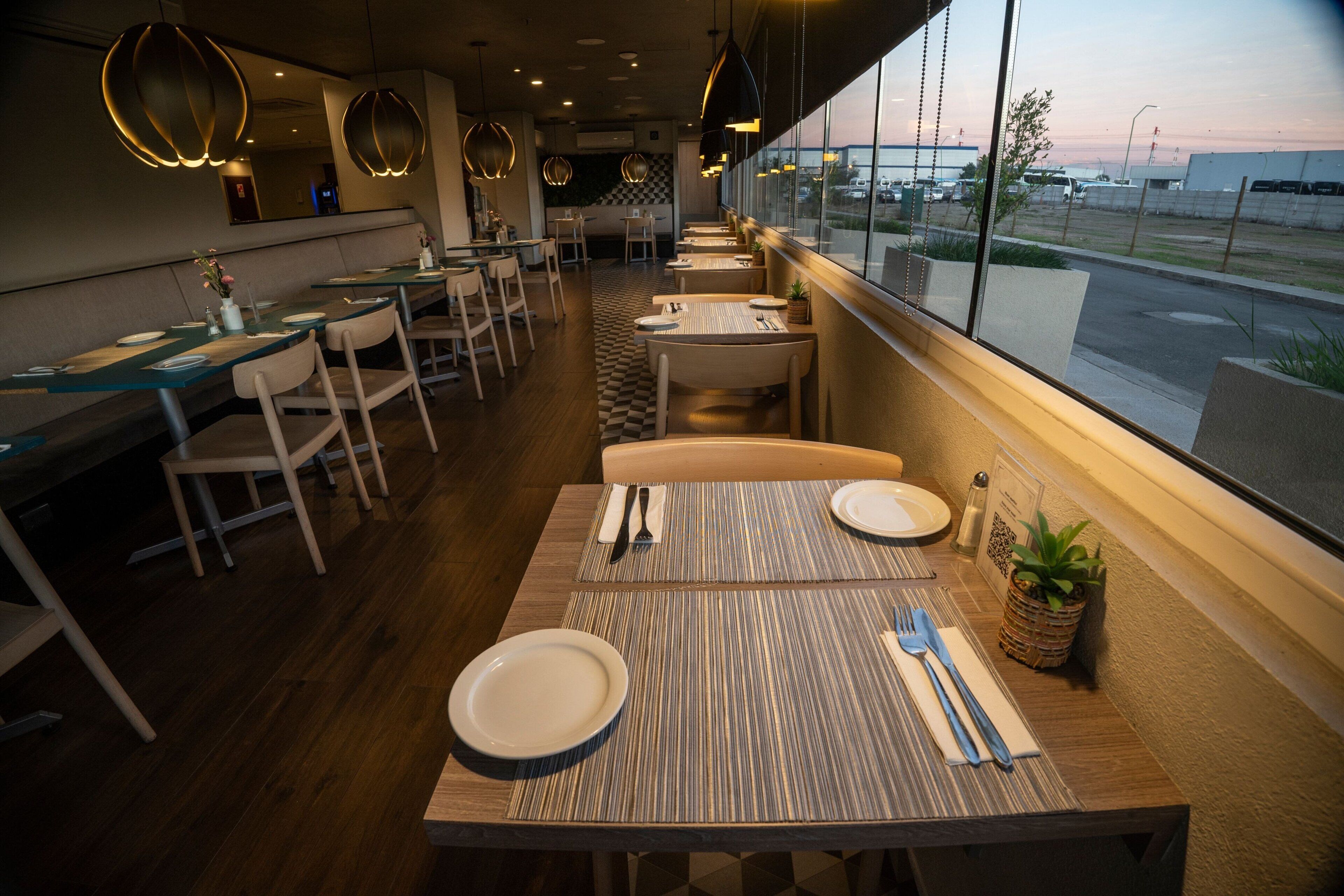 Un restaurant avec des tables et des chaises en bois, un sol à carreaux et de grandes fenêtres donnant sur un parking.