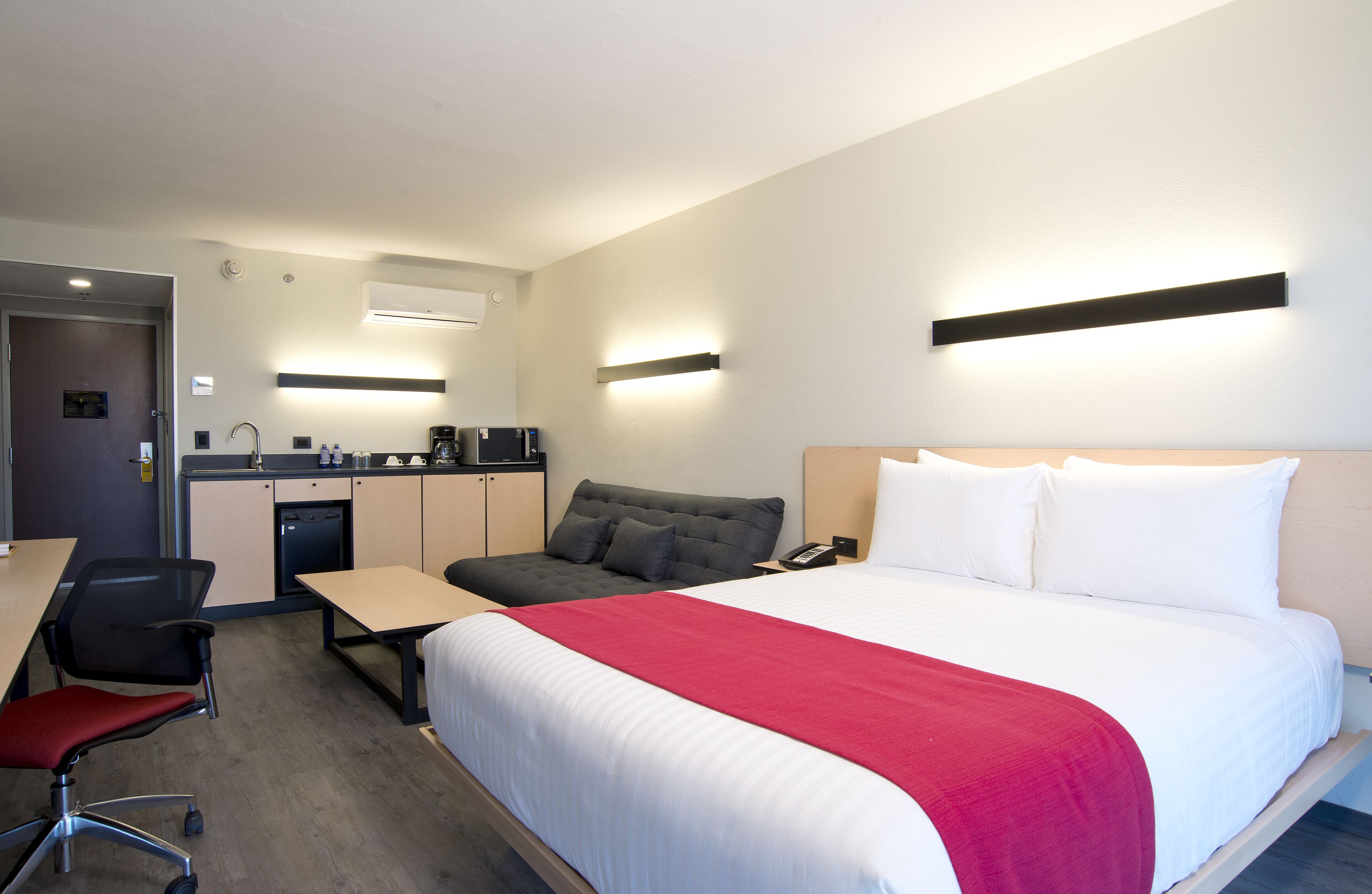 Habitación de hotel con cama, escritorio, silla, kitchenette y sofá.