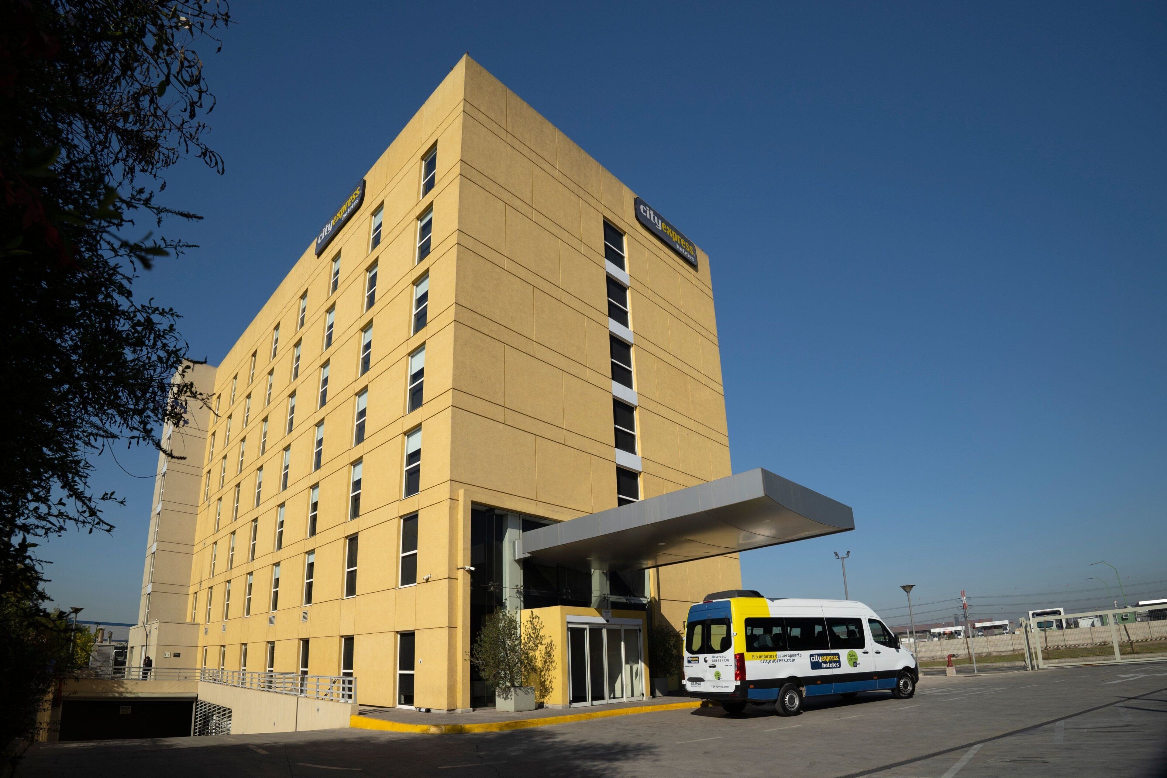 A hotel with a yellow facade, a covered entrance, and a van parked in front.