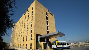 A hotel with a yellow facade, a covered entrance, and a van parked in front.