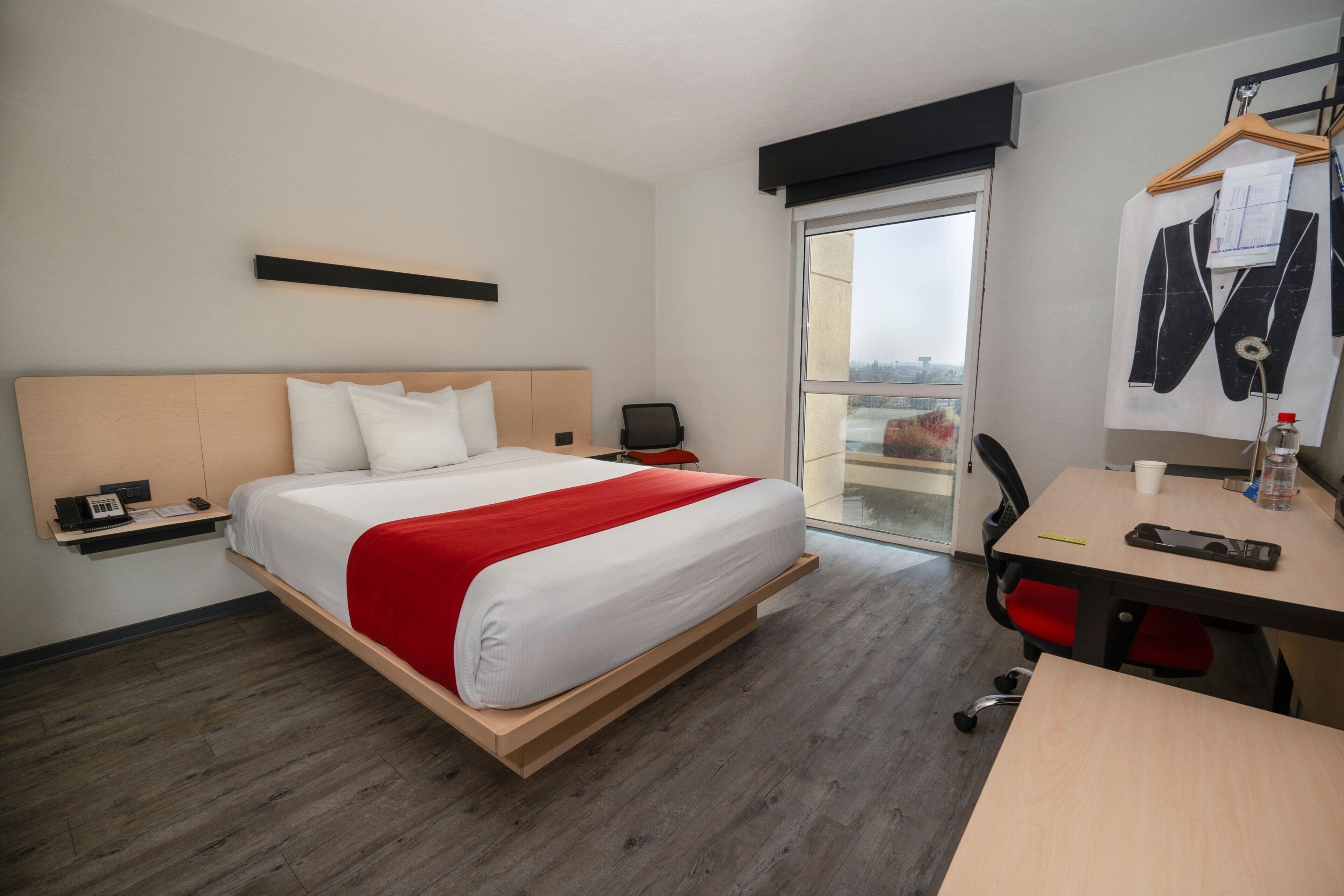 Camera d'albergo con un letto, una scrivania, una sedia, un appendiabiti e vista sulla città dalla finestra.
