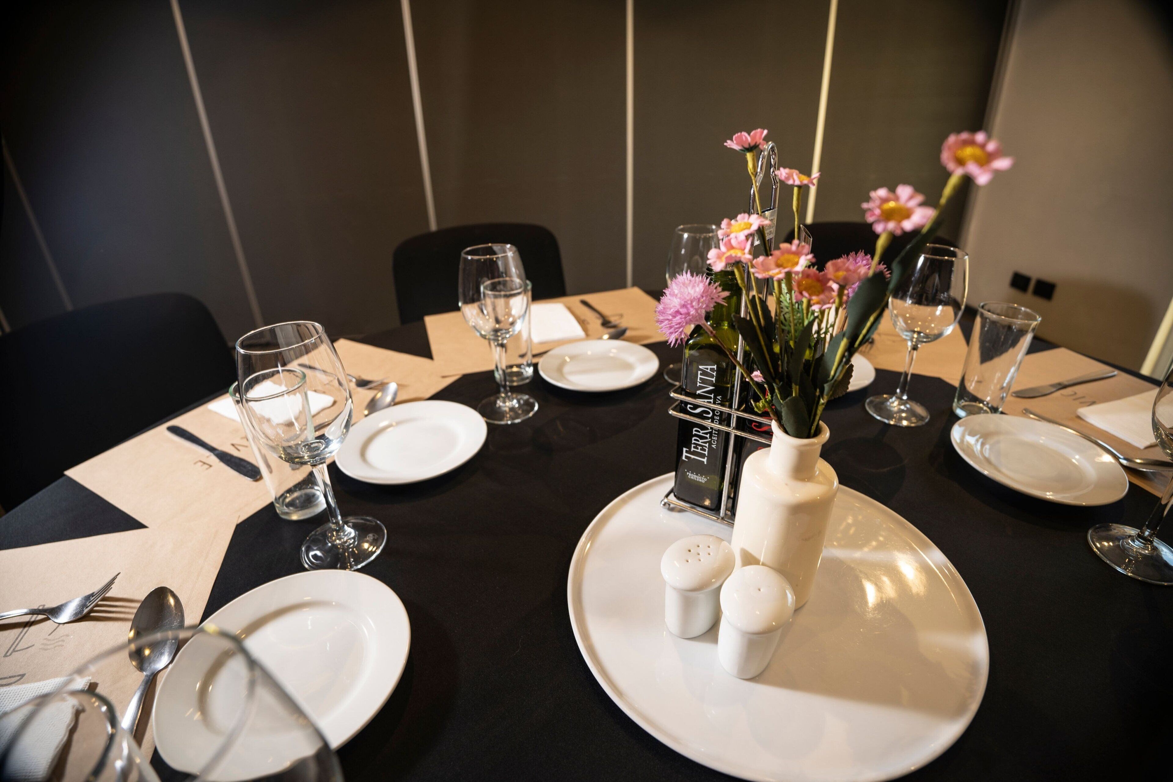 Une table mise pour le repas, avec des assiettes, des couverts, des verres et un vase rempli de fleurs.