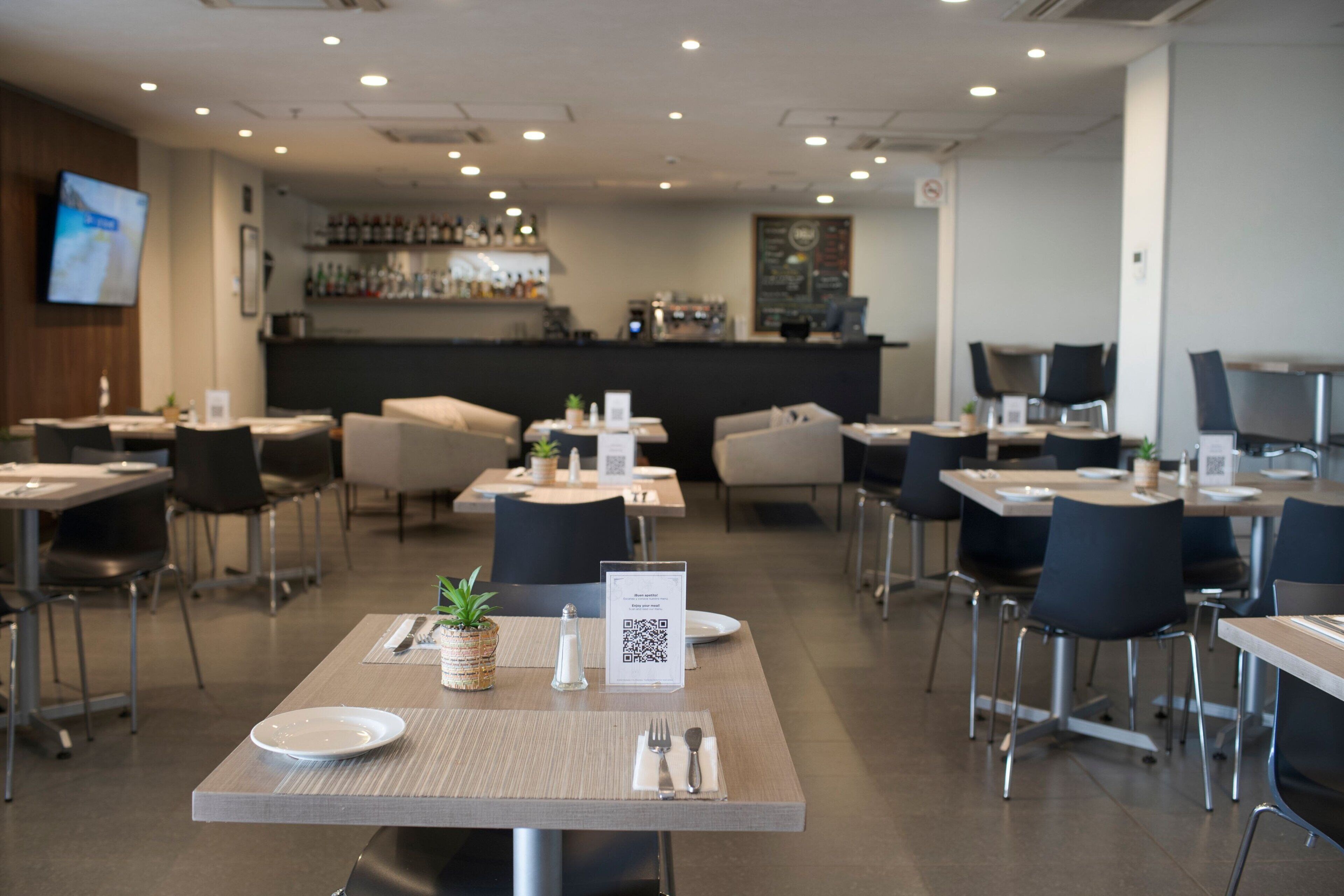 Un restaurante moderno con mesas dispuestas para comer, una zona de bar al fondo y un código QR sobre la mesa.