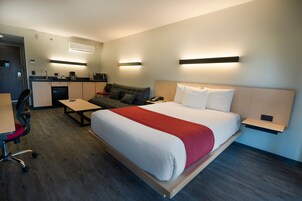 A hotel room with a bed, a desk, a chair, a sofa, and a kitchenette.