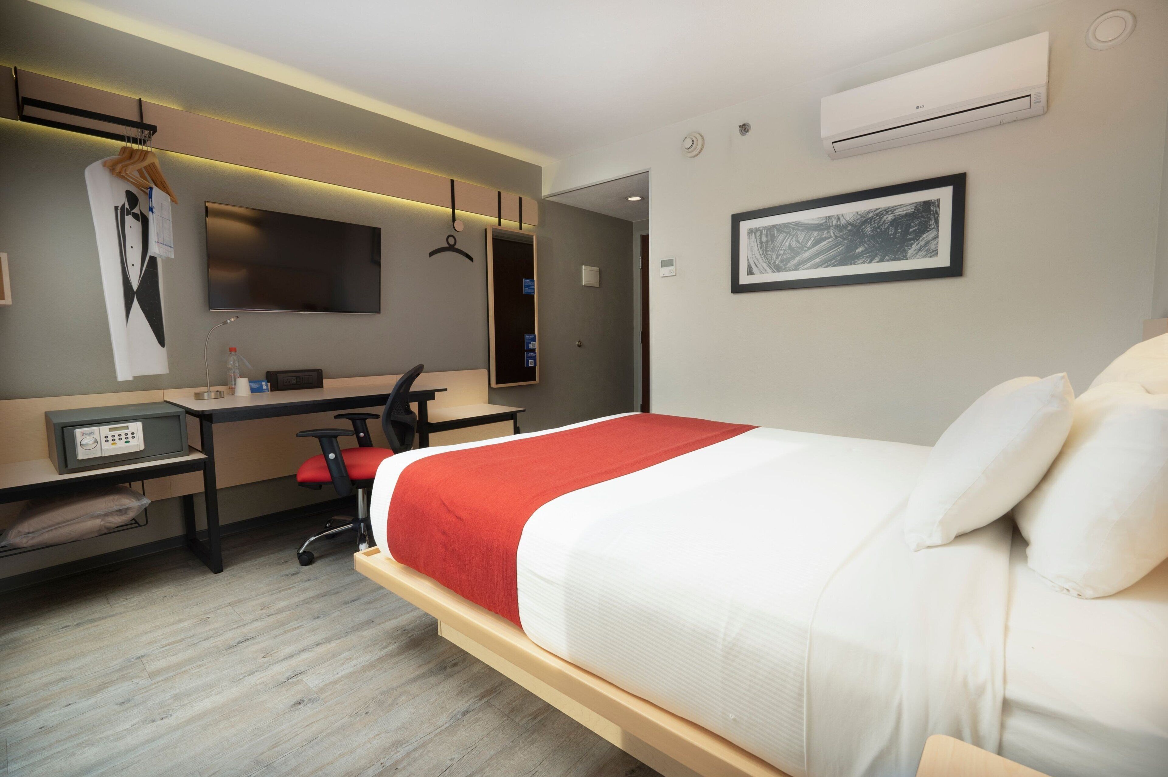 A hotel room with a bed, desk, chair, and a TV.