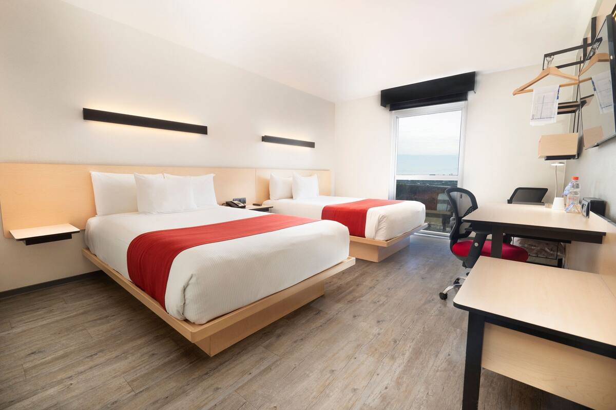 A hotel room with two beds, a desk, and a chair.
