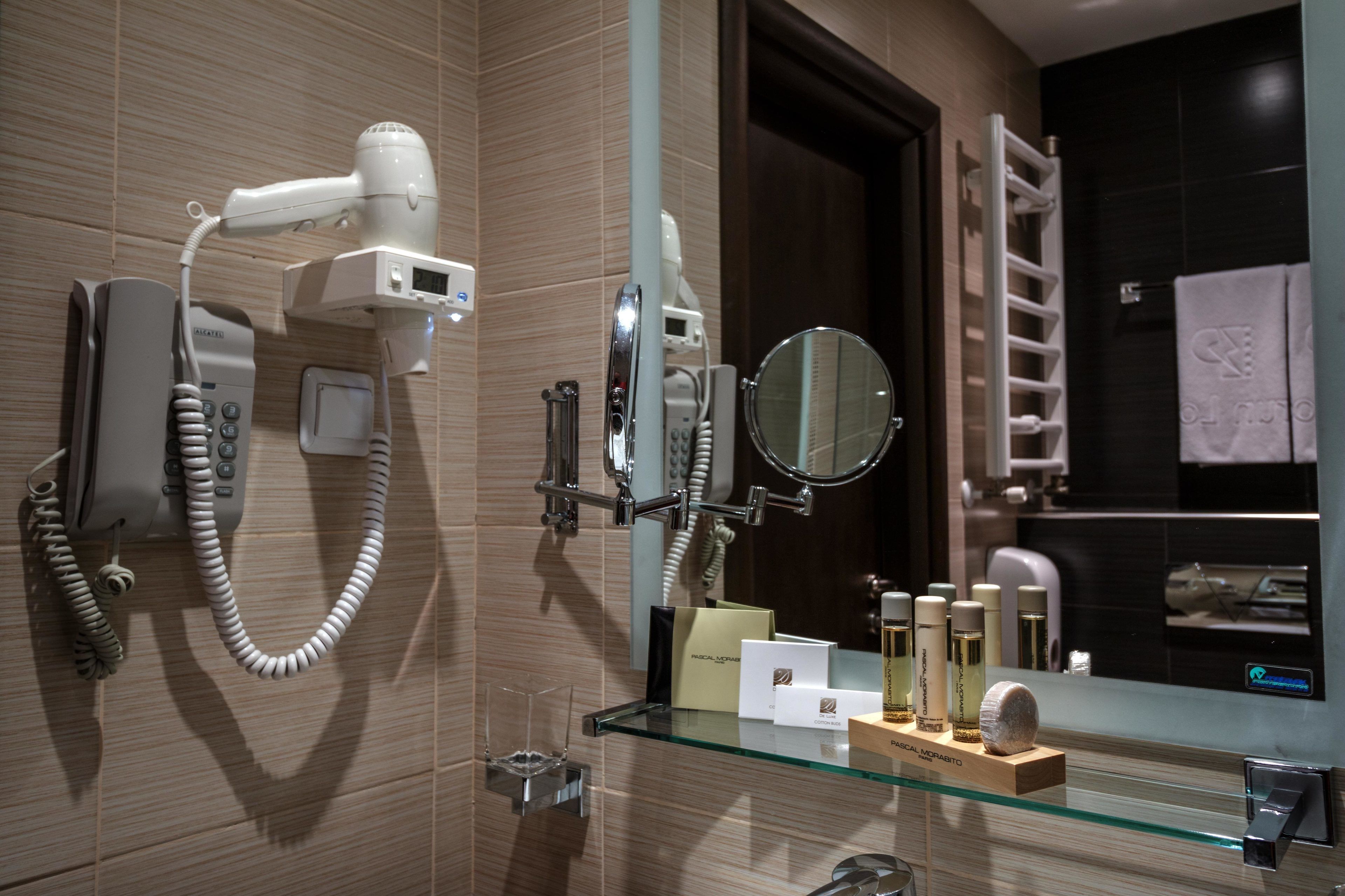 Een badkamer met een haardroger, een spiegel en een glazen plank met toiletartikelen.