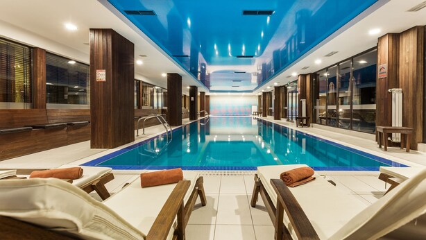 A modern indoor swimming pool with lounge chairs and wooden accents. - Perun Lodge Hotel (Bansko)