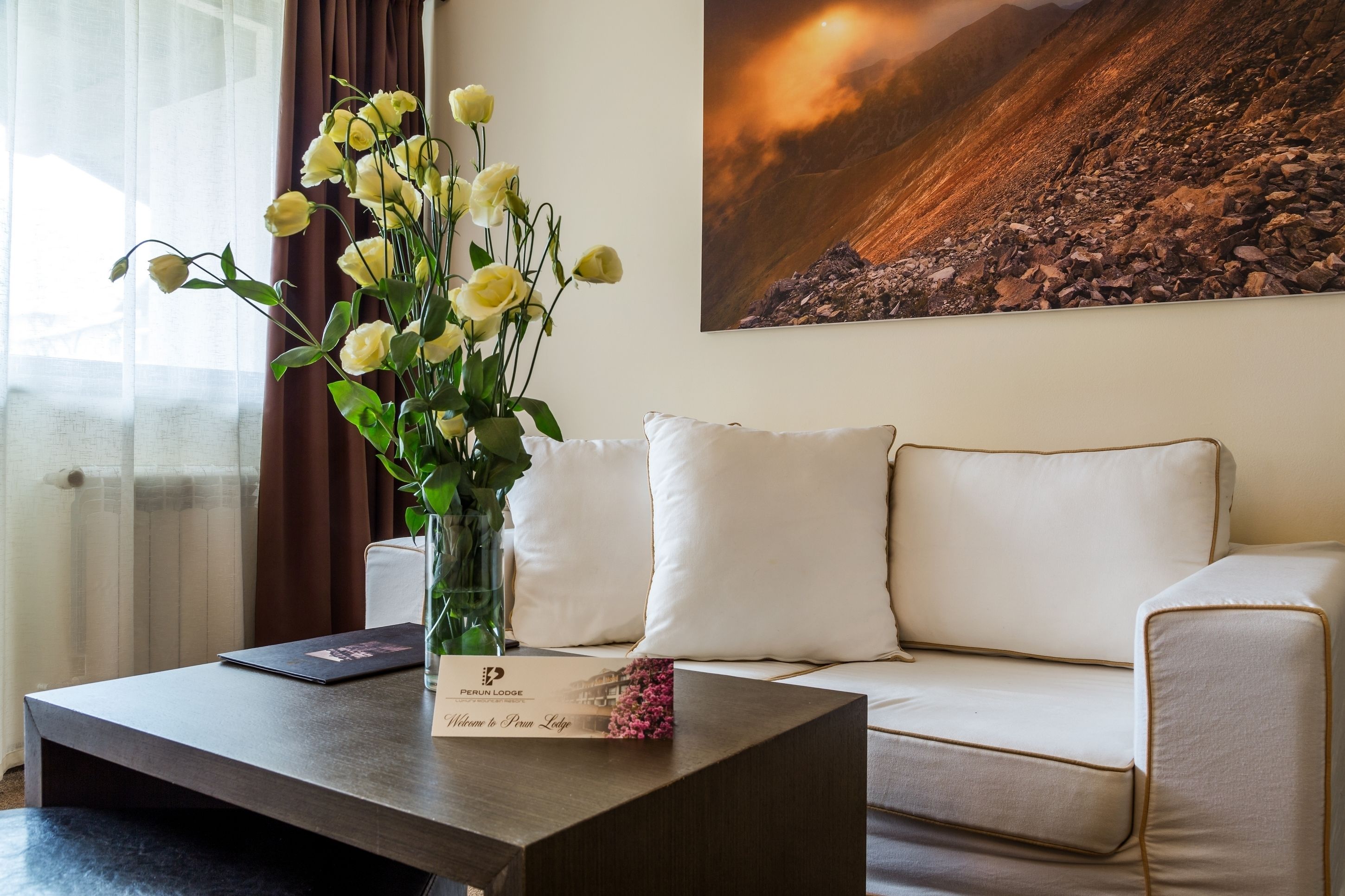 A modern hotel room with a sofa, a coffee table with a vase of flowers, and a framed picture on the wall.