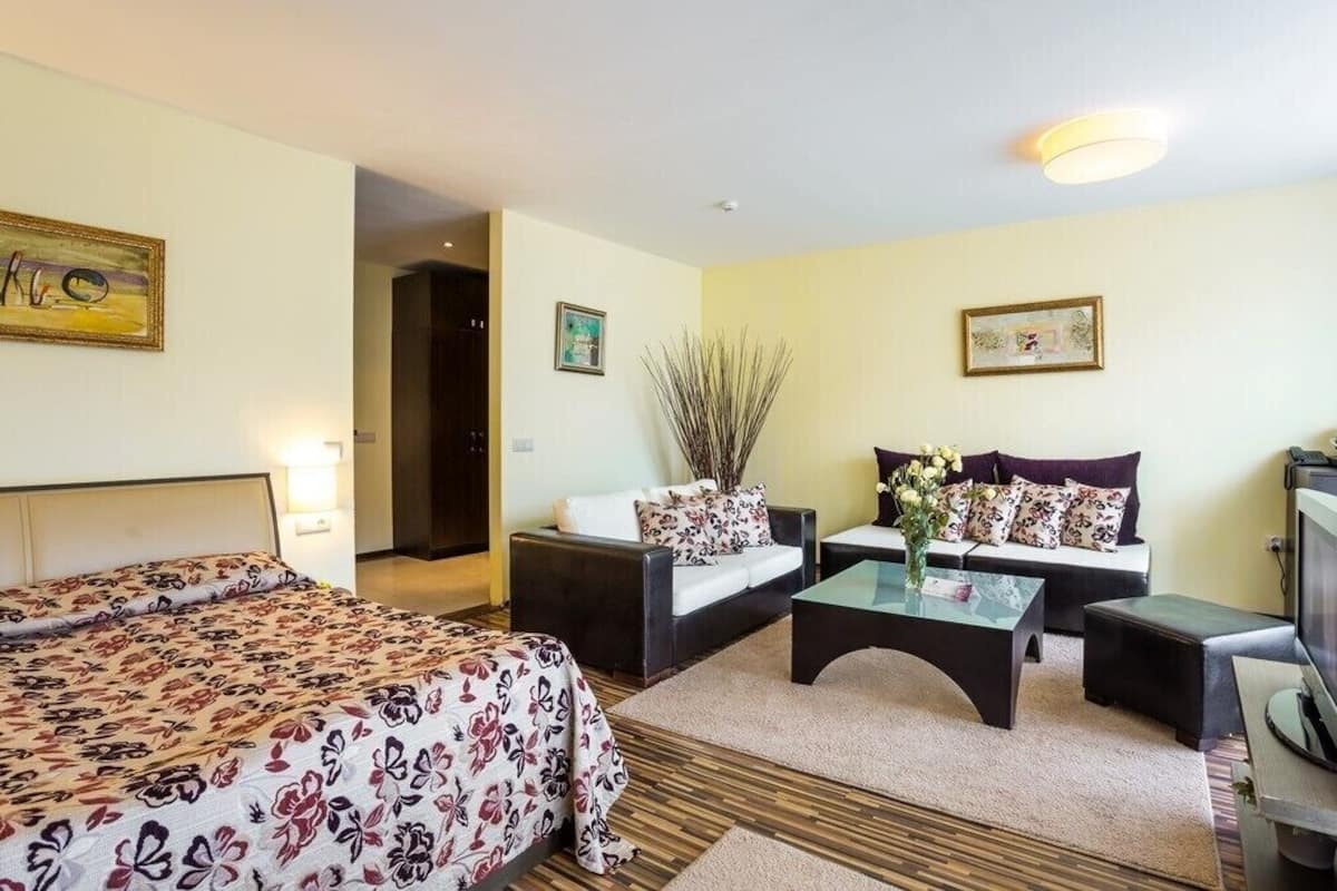 Una habitación de hotel con cama, dos sofás, una mesa de centro y televisor.