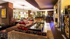 A spacious living area with sofas, a coffee table, and a fireplace. There is a bar area in the background with a television and bookshelves. - Perun Lodge Hotel (Bansko)