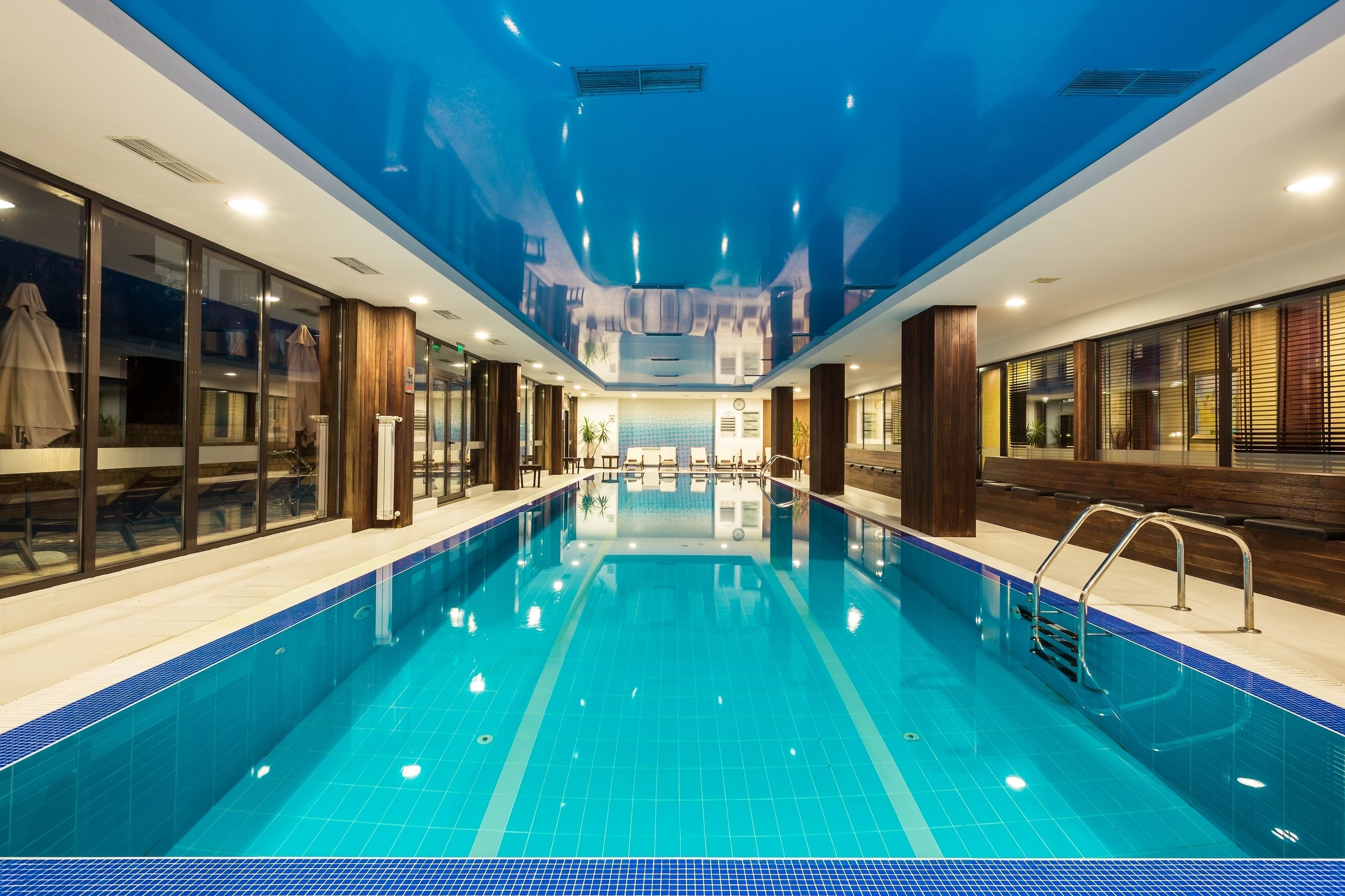 Una gran piscina coberta amb aigua cristal·lina blava, envoltada de parets de vidre i panells de fusta.