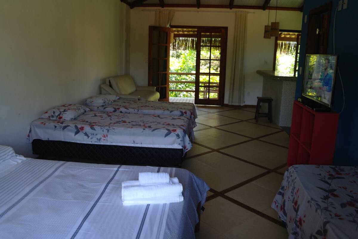 A hotel room with two beds, a TV, and a view of greenery outside.