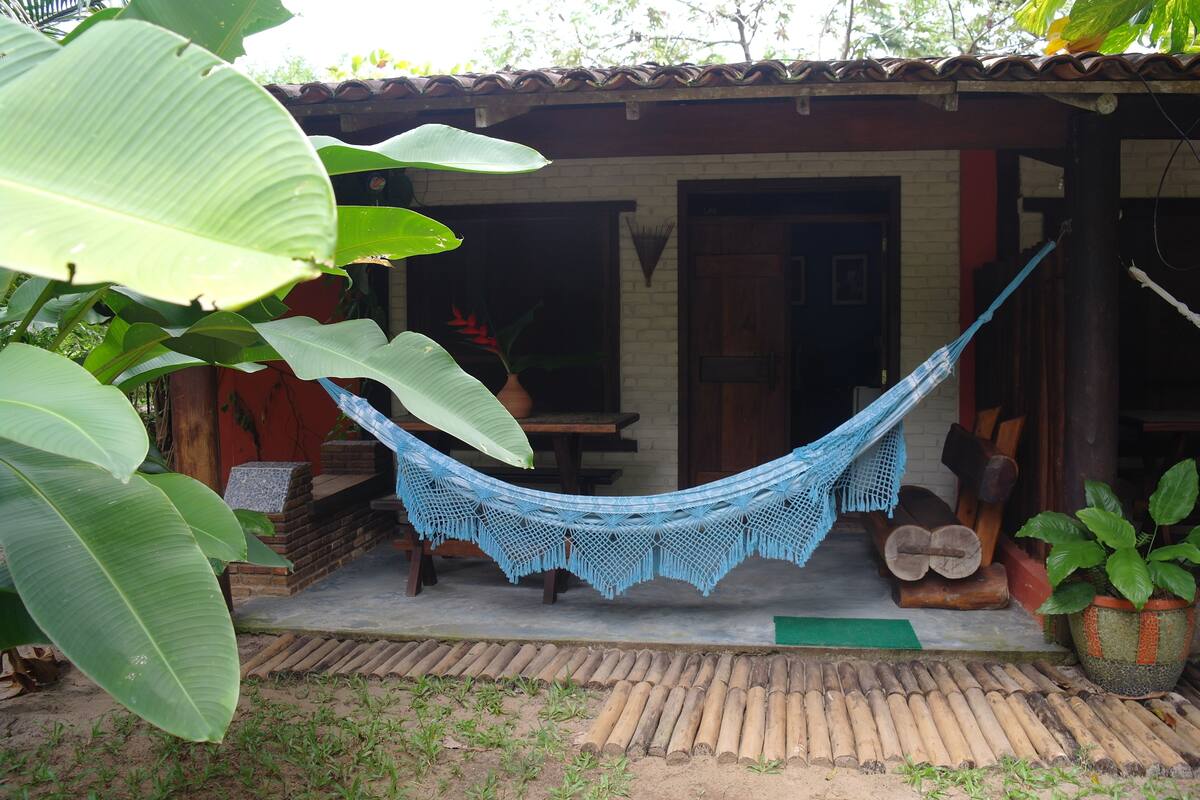 A hammock tied between a wooden structure and a brick wall, with a potted plant and logs nearby.