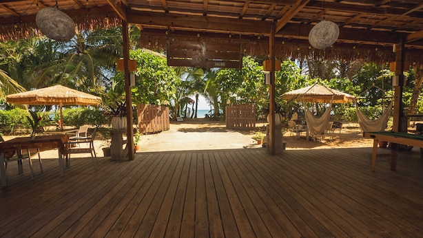 An outdoor wooden deck with thatched umbrellas, a hammock, and a wooden fence leading to a beach. - Playa Bluff Hotel (Bocas del Toro)