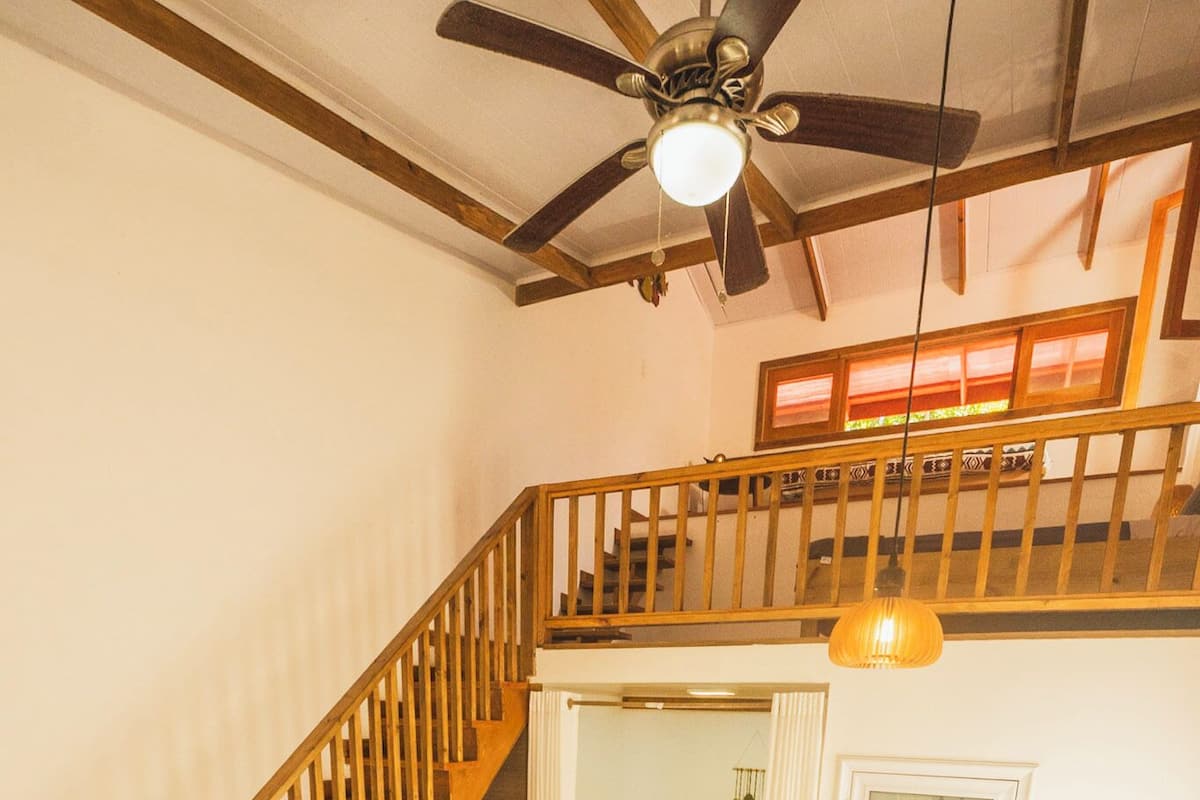 Un loft amplio con escalera de madera, ventilador de techo y una cama grande con vistas al exterior.