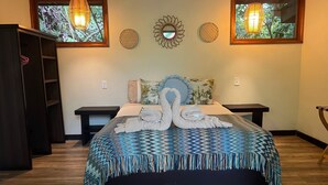 A neatly made bed with a blue and green patterned bedspread, two wall-mounted lamps, and a decorative mirror above the bed. - Playa Bluff Hotel (Bocas del Toro)
