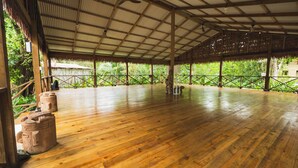 A spacious indoor area with a high ceiling and wooden flooring, surrounded by lush greenery. - Playa Bluff Hotel (Bocas del Toro)