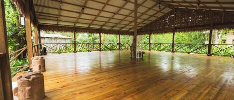 A spacious indoor area with a high ceiling and wooden flooring, surrounded by lush greenery.