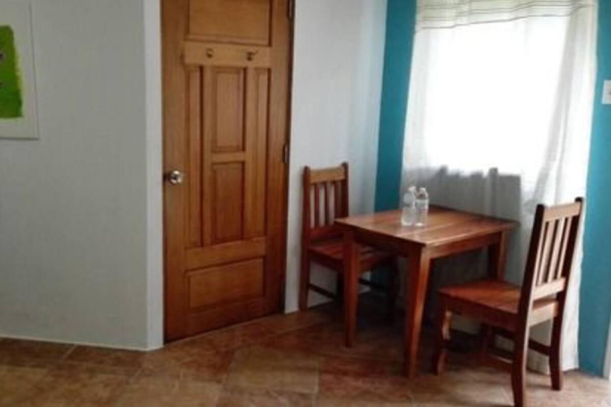Una habitación con puerta de madera, una mesa pequeña con sillas y piso de baldosas.