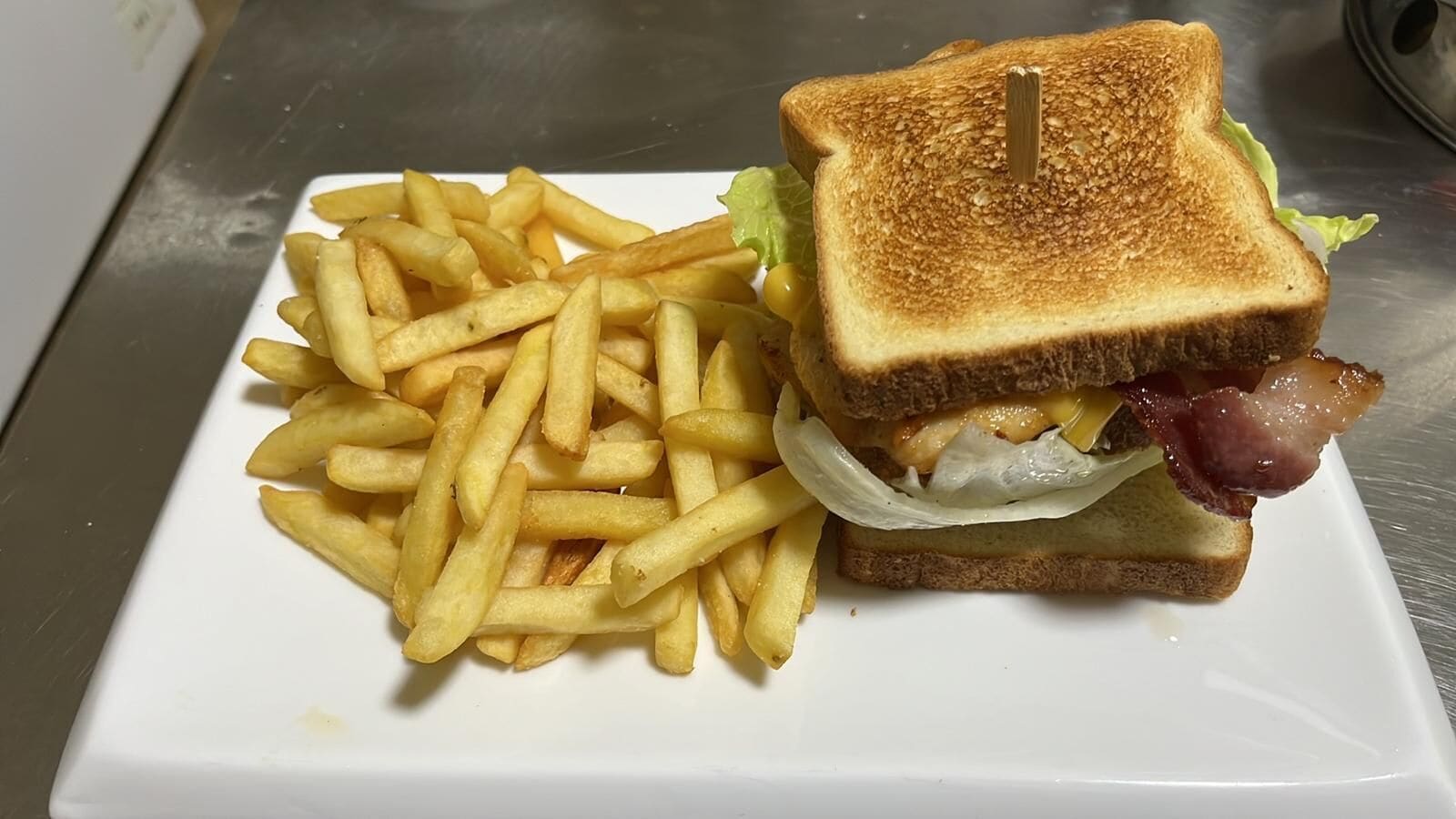 Sándwich con tocino, lechuga y queso, acompañado de papas fritas sobre un plato blanco.