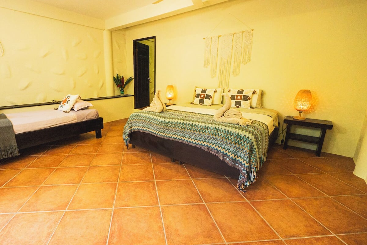 Una habitación con dos camas, un espejo, una lámpara de pared y una mesita pequeña.