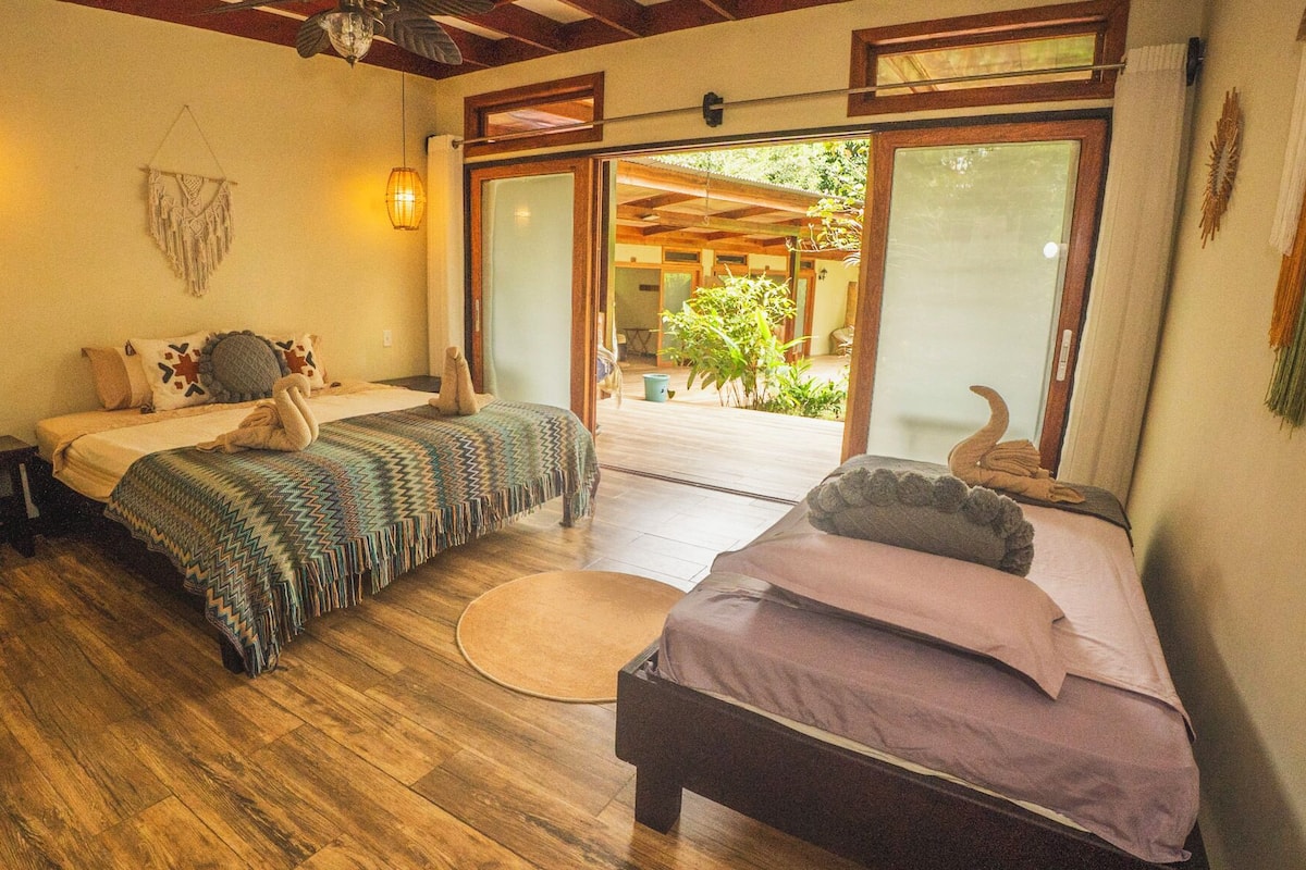 Un dormitorio acogedor con dos camas, suelo de madera y vistas a un jardín a través de un ventanal corredero.