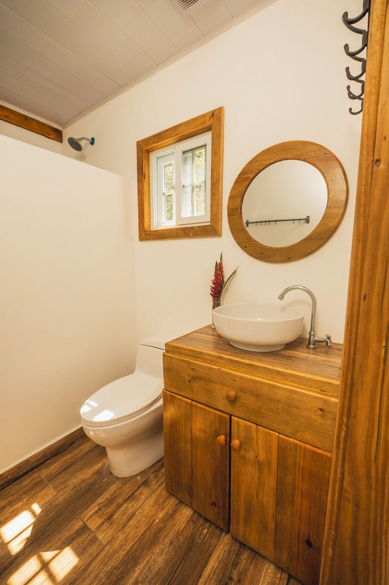 Un baño con tocador de madera, espejo redondo, lavamanos blanco y retrete.