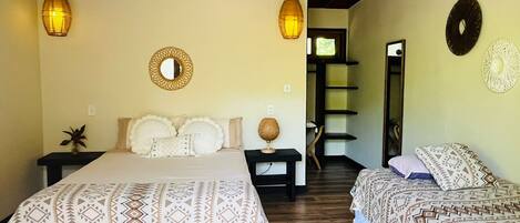 A bedroom with two beds, wooden flooring, a ceiling fan, and a mirror on the wall.