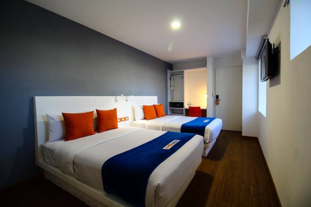 A hotel room with two beds, a TV, and a small kitchenette.